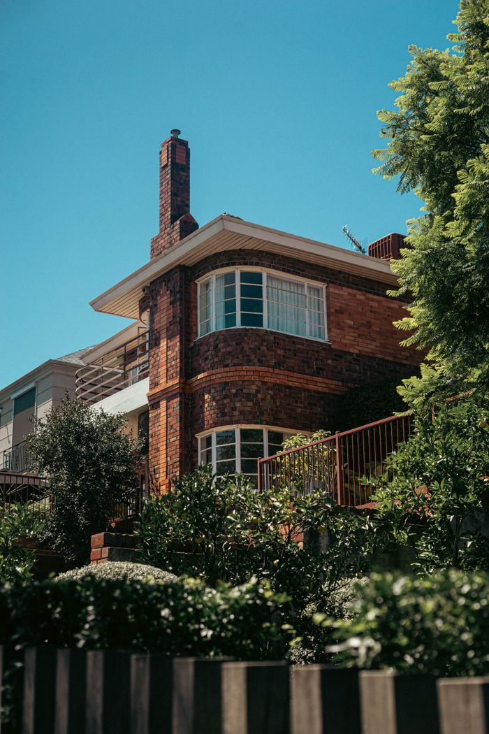 home-services-03 A picturesque brick house surrounded by lush greenery under a bright blue sky, capturing serene residential architecture.